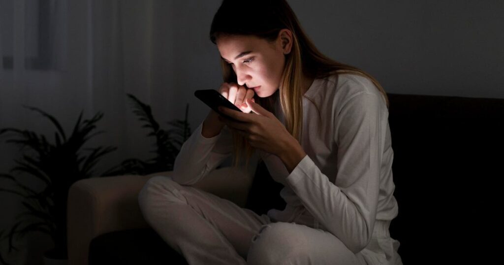 Nő sötét szobában telefonját nézi éjszaka – digitális túlterheltség és telefonfüggőség jelei